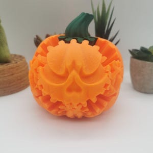 Könnte beinhalten: Ein orangefarbener Kürbis mit einem geschnitzten Gesicht und einem grünen Stiel. Der Kürbis hat ein detailliertes Design, perfekt für Halloween-Dekorationen. Der Kürbis steht auf einer weißen Oberfläche.