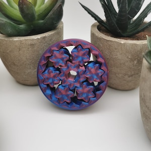 Può includere: Un ingranaggio rotondo in metallo blu e rosa con un motivo a forma di stella. L'ingranaggio è in metallo e ha una finitura lucida.