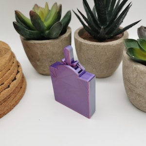 Könnte beinhalten: Eine kleine, violette, 3D-gedruckte Box mit einem Scharnierdeckel. Die Box hat eine strukturierte Oberfläche und ein kleines, dekoratives Detail auf der Oberseite.