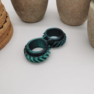 Op de afbeelding: Een teal en zwart fidget-speelgoed met een tandwielontwerp. Het speelgoed is gemaakt van plastic en heeft twee ringen die onafhankelijk van elkaar draaien.