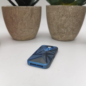 Könnte beinhalten: Eine blaue Handyhülle mit geometrischem Muster. Die Hülle hat ein dunkelblaues und graues Muster mit einem hellblauen Rand.