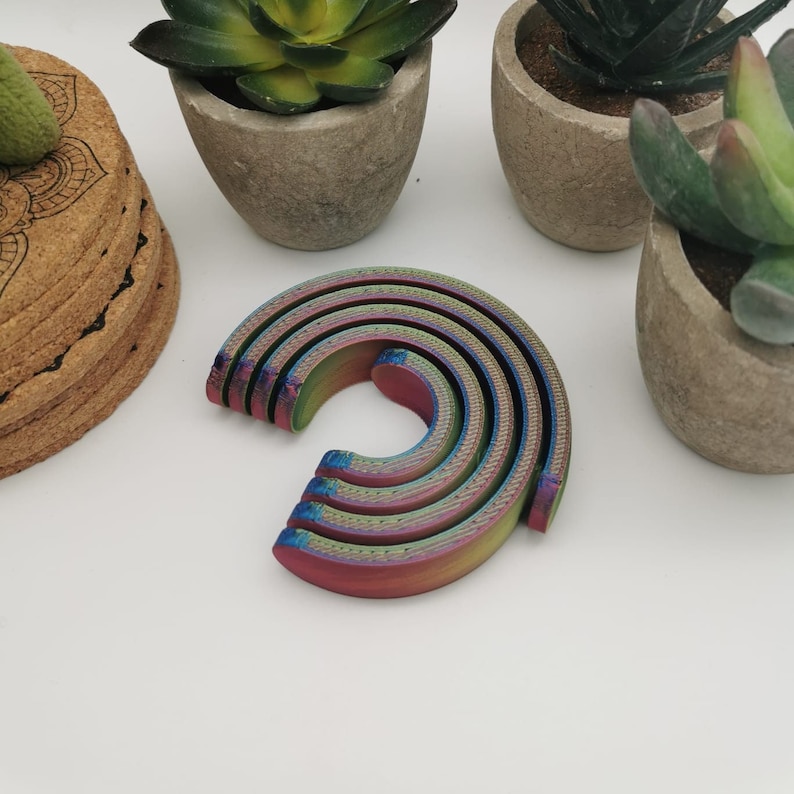 Puede incluir: Un conjunto de cinco anillos de madera semicirculares, entrelazados y con colores de arco&iacute;ris. Los anillos est&aacute;n apilados uno encima del otro, creando un arco&iacute;ris.