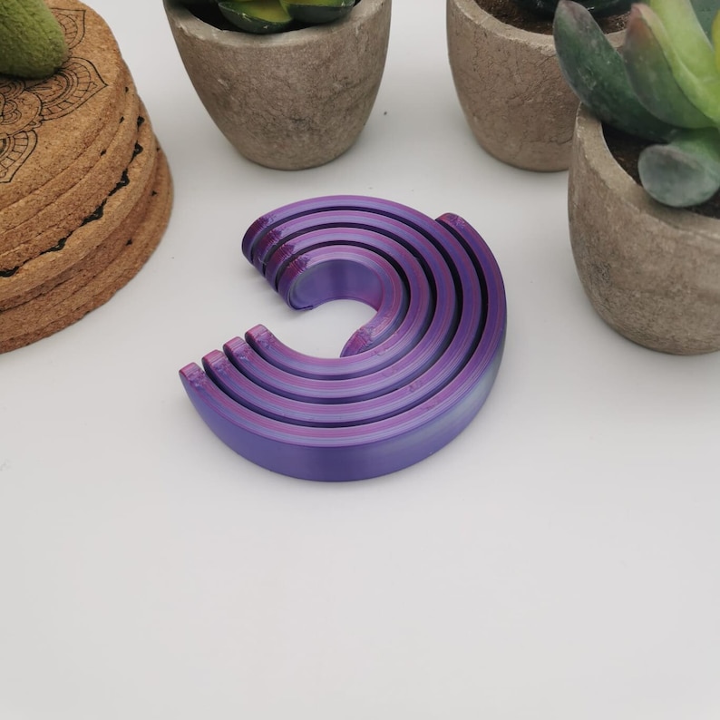 Puede incluir: Conjunto de cinco anillos de pl&aacute;stico morado e iridiscente, apilados en c&iacute;rculo.