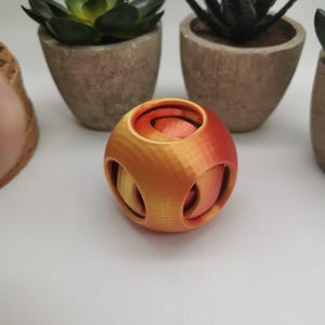 May include: A 3D printed ball with a geometric design. The ball is made of orange and red plastic and has a textured surface.