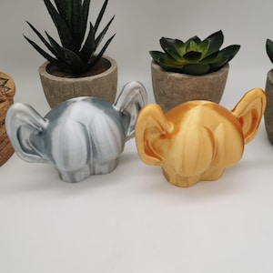 Può includere: Due figurine di orecchie stampate in 3D, una è bianca e l'altra è dorata.