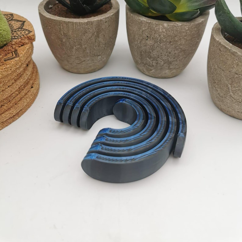 Puede incluir: Un conjunto de cinco anillos entrelazados azules y negros, apilados en forma de semic&iacute;rculo. Los anillos est&aacute;n hechos de un material liso y texturizado.