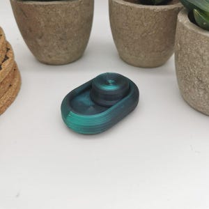 May include: A teal and green oval-shaped dish with a smaller teal and green round dish inside. The dishes are made of a smooth, textured material.