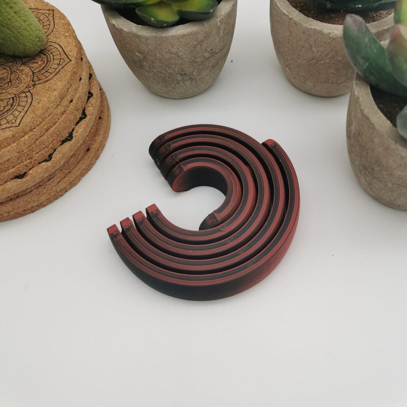 Puede incluir: Un conjunto de seis anillos de anidaci&oacute;n de color rojo y negro. Los anillos est&aacute;n hechos de un material liso y duro y est&aacute;n dispuestos en un c&iacute;rculo.
