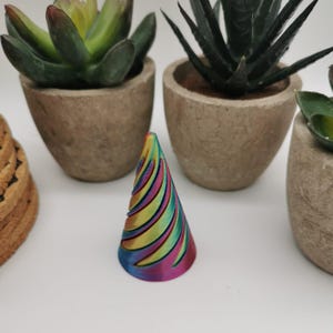 May include: A colourful, iridescent cone with a swirling pattern. The cone is made of a smooth, shiny material and has a rounded top.