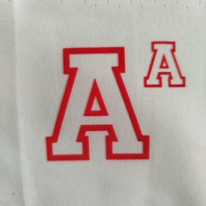 Op de afbeelding: Witte stof met een grote rode letter "A" en een kleinere rode letter "A" rechtsboven. De letters hebben een blokstijl met een witte omtrek.