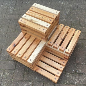 May include: A wooden step stool made of stacked wooden planks with rounded edges. The stool is made of natural wood with a light brown colour and has a rustic look. The stool has a three-step design with a square top step and two rectangular steps below.