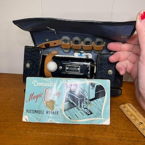 May include: A vintage black leather case with a small sewing machine inside. The sewing machine is labeled "Domestic Magic Key Buttonhole Worker".