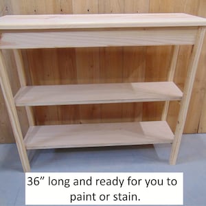 May include: A 36-inch long unfinished wooden shelf unit with three shelves. The shelf unit is made of natural wood and is ready to be painted or stained.