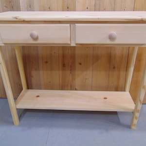 May include: A natural wood console table with two drawers and a lower shelf. The table has a simple design with rounded drawer pulls.