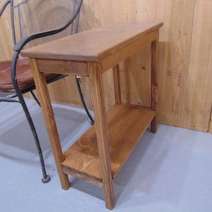 May include: A small wooden end table with a shelf. The table is stained a dark brown color and has a simple design.
