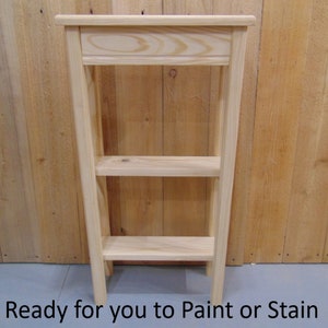 May include: A wooden shelf unit with three shelves. The shelf unit is made of unfinished wood and is ready to be painted or stained.
