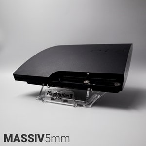 Könnte beinhalten: Eine schwarze PlayStation 3 Slim Konsole auf einem transparenten Acryl-Ständer. Der Ständer trägt den Text "PlayStation 3 Slim". Die Konsole steht auf einer weißen Oberfläche. MASSIV5mm