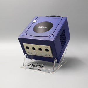 Op de afbeelding: Een paarse Nintendo GameCube console met een transparante acryl standaard. De console heeft een zwart schijfstation en een wit label met de tekst "Nintendo GameCube".