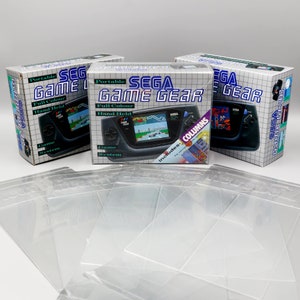 Peut inclure: Trois boîtes scellées d'une console de jeu vidéo portable Sega Game Gear. Chaque boîte présente une Game Gear noire et grise avec un écran affichant un jeu de course. Les boîtes sont blanches avec des accents bleus et rouges. Le texte sur les boîtes indique "Sega Game Gear" et "Système de jeu portable couleur pleine main".
