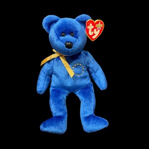 May include: Blue Ty Beanie Baby with a yellow ribbon and a European Union symbol on its chest. The tag reads "Ty" and "Beanie Babies".