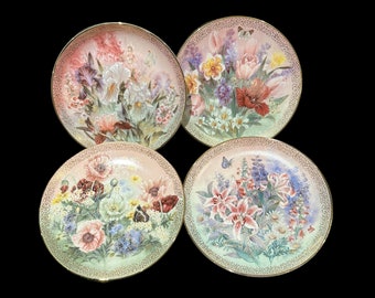 May include: Set of four decorative plates featuring floral designs. Each plate has a different floral arrangement with butterflies and a gold rim.