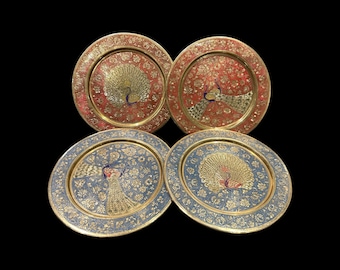May include: Four decorative brass plates featuring peacock designs. The plates have a gold rim and are decorated with intricate floral patterns. Two plates have a red background and two plates have a blue background.