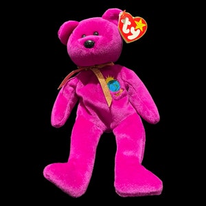 May include: A pink Beanie Baby with a gold ribbon and a patch that says "Ty Inc. 1993-1999" with a globe on it. The Beanie Baby has a red Ty tag with a white star.