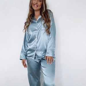 May include: A light blue satin pajama set with long sleeves and pants. The top has a button-up front and a pocket on the left chest.