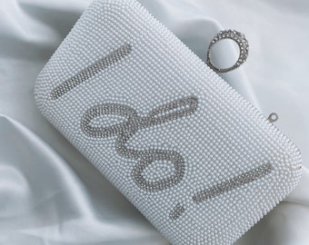 Peut inclure: Une pochette blanche en perles avec un motif argenté 'I Do' et une bague en strass argent.