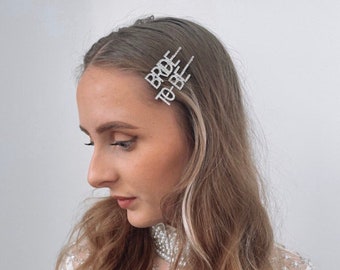 May include: Three silver hair clips with rhinestones spelling out "Bride to Be".