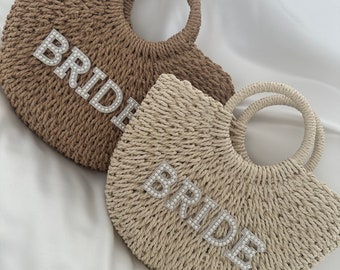May include: Two straw tote bags with a pearl embellished "BRIDE" design. One bag is brown and the other is beige.