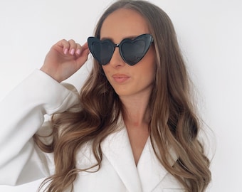 May include: A woman wearing a white blazer with a black heart-shaped sunglasses.