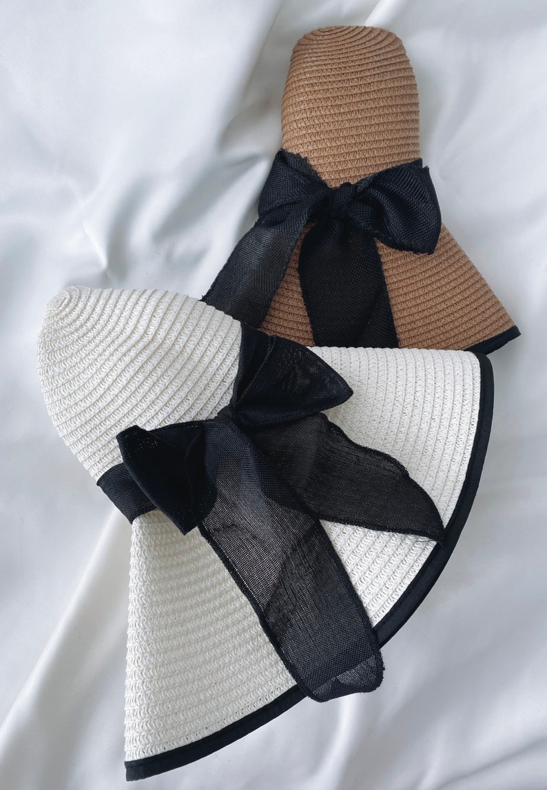May include: Two straw sun hats with wide brims and black ribbon bows. The hats are in different colors, one is white and the other is brown.
