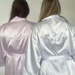 May include: A set of three ceramic mugs with a speckled, cream-colored glaze. Each mug features a different hand-painted floral design in shades of blue, green, and yellow. The mugs have a simple, rounded shape and a comfortable handle.