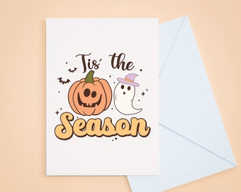 May include: A white card with a pumpkin and ghost illustration. The text on the card reads "Tis' the Season."