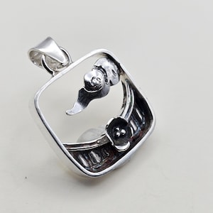 May include: A silver pendant with a square frame and floral design. The pendant features a flower and leaf motif within the frame, with a bail for a chain. The pendant is made of a shiny, reflective metal.