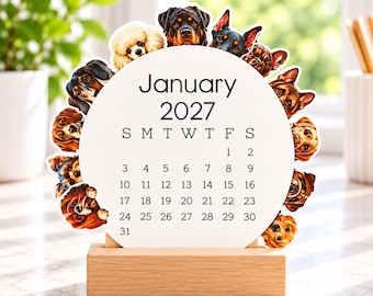 May include: A circular January 2027 calendar printed on white cardstock, featuring a border of various dog breeds. The calendar is held upright by a rectangular light-colored wooden base, displaying the month, year, and days of the month.