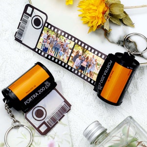 May include: A personalized film strip keychain with a family photo, alongside a film canister keychain. The film canister is orange and black, with "Portra 200-36" printed on it. The film strip shows a group of people.
