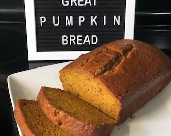 Puede incluir: Un tablero de letras blanco con el texto "WELCOME GREAT PUMPKIN BREAD" y una hogaza de pan de calabaza cortada en rodajas en un plato blanco.
