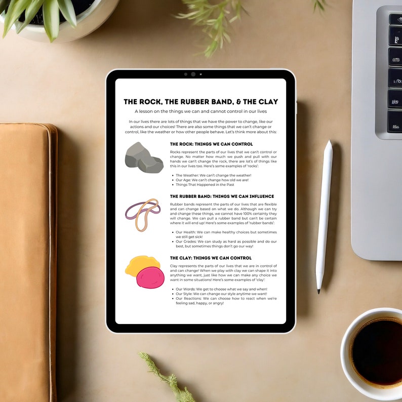 May include: A digital tablet displays a lesson titled "THE ROCK, THE RUBBER BAND, & THE CLAY." The lesson uses visual aids of rocks, rubber bands, and clay to illustrate concepts of control and influence. A stylus and a coffee cup are also visible.