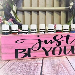 May include: Pink wooden essential oil holder with the text "Just Be You" and 10 clear glass bottles with white lids.