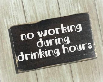 May include: A black wooden sign with white text that reads "no working during drinking hours".