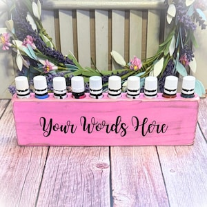 May include: Pink wooden essential oil holder with ten slots for bottles. The holder has the words "Your Words Here" written on the front.