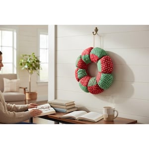 May include: A handmade wreath with alternating sections of red and green fabric, each patterned with white dots or small flowers. The wreath is hanging on a white wall, adding a touch of festive decor to the space.