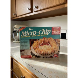 May include: A box for a Micro-Chip microwave potato chip maker. The box is teal and red with the words "Micro-Chip" in large letters. The box advertises delicious, crispy, fat-free potato chips. The box also shows a picture of chips.