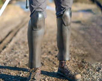 May include: A person wearing gray pants with a black belt and black knee-high boots. The boots have a silver metal panel on the front.