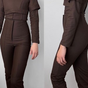 May include: A brown jumpsuit with a high waist and long sleeves. The jumpsuit has a fitted bodice and wide legs.