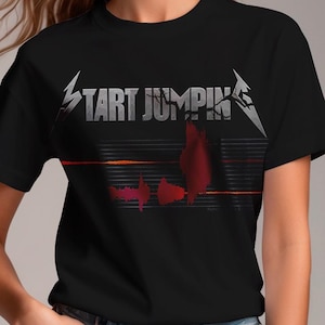 May include: Black t-shirt with the text "START JUMPIN'" in silver and a red graphic design. The shirt has a crew neck and short sleeves. The website address "wickedcat.co" is in the bottom left corner.