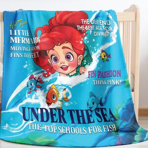 May include: A blue and pink blanket featuring a cartoon mermaid, fish, and the text "Hot Topic Little Mermaids Moving From Fins To Feet The Deep End The Best Age For Diving In Fin Fashion Think Pink! Under The Sea The Top Schools For Fish"