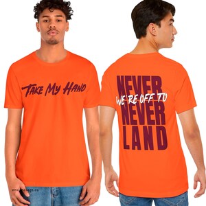 May include: Orange t-shirt with the text "Take My Hand" printed on the front and "Never We're Off To Never Land" printed on the back in maroon.